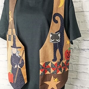 Może przedstawiać: Kamizelka bez rękaw&oacute;w z patchworkowym wzorem z motywami Halloween. Tkanina przedstawia czarownicę z miotłą, czarnego kota, ż&oacute;łty p&oacute;łksiężyc, dynię i gwiazdy. Kamizelka posiada brązowe panele w kratkę oraz inne wzorzyste elementy.