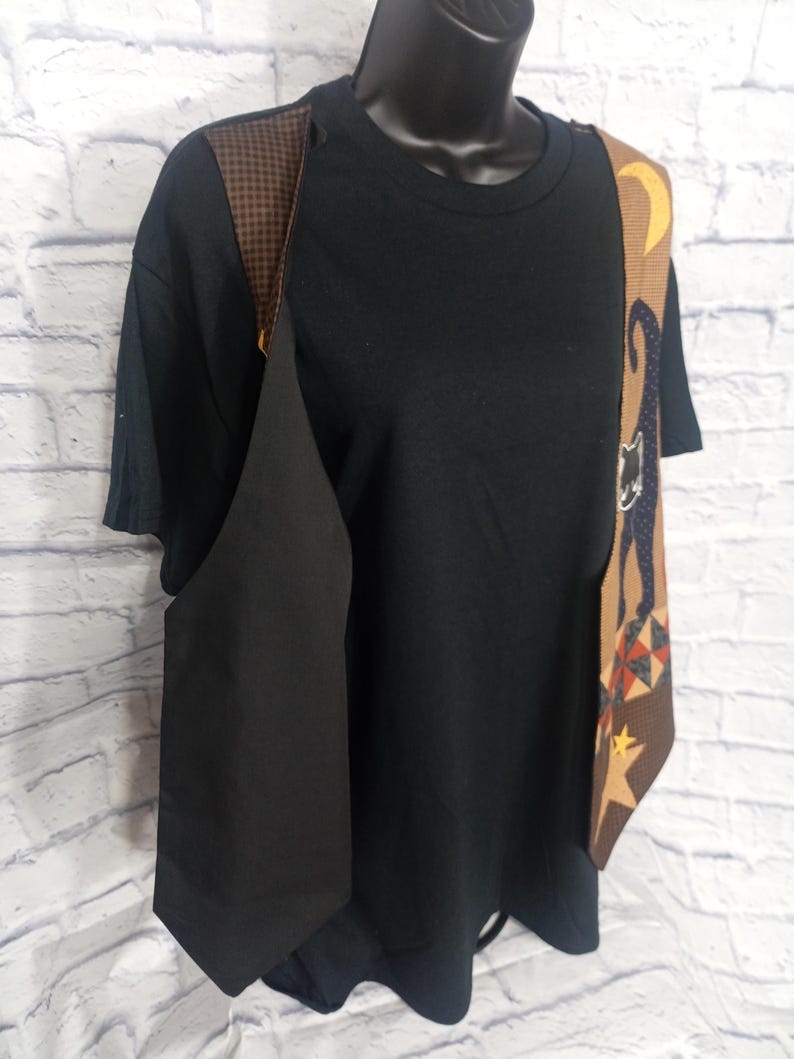 Może przedstawiać: Czarny t-shirt pod kamizelką z brązowym panelem przedstawiającym sylwetkę czarnego kota, ż&oacute;łty p&oacute;łksiężyc i ż&oacute;łtą gwiazdę. Kamizelka posiada brązowo-czarną kratkę na ramionach oraz geometryczny wz&oacute;r w romby.