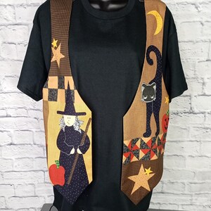 Może przedstawiać: Czarny t-shirt z kr&oacute;tkim rękawem noszony pod bezrękawnikiem z patchworkowym wzorem. Kamizelka przedstawia czarownicę z miotłą, czarnego kota, ż&oacute;łty p&oacute;łksiężyc, gwiazdy, czerwone jabłko i dynię na brązowym materiale.