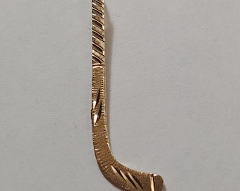 Könnte beinhalten: Ein goldfarbener Hockey-Schlüsselanhänger. Der Anhänger ist mit einem strukturierten Design verziert.