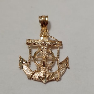 May include: A gold-toned anchor pendant with a detailed design. The anchor features a figure of Jesus Christ on a cross, surrounded by a wheel.