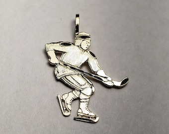 Könnte beinhalten: Ein goldfarbener Anhänger, der einen Eishockeyspieler beim Schlittschuhlaufen mit einem Schläger zeigt. Der Spieler trägt einen Helm und Schlittschuhe.