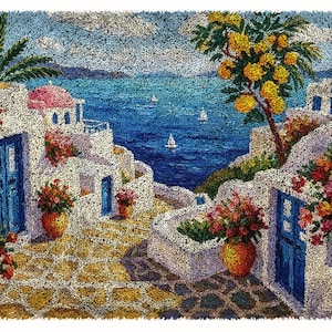 May include: A textured rug featuring a Mediterranean coastal scene with white buildings, blue doors, and pink flowers. The landscape includes a stone path, a tree with yellow blossoms, and a deep blue sea with small white sailboats under a sky.
