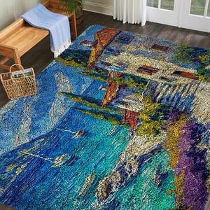 May include: A large, rectangular area rug with a vibrant, impressionistic design. The rug depicts a coastal scene with a building, water, and boats, using shades of blue, green, yellow, and purple. The rug is placed on a dark wood floor.