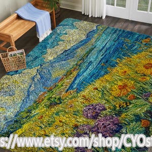 May include: A large, colorful rug with a landscape design. The rug features a vibrant mix of blues, greens, yellows, and purples, depicting a mountain scene with flowers. The rug is placed on a dark wood floor, with a bench and basket in the background.