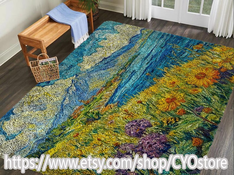 May include: A large, colorful rug with a landscape design. The rug features a vibrant mix of blues, greens, yellows, and purples, depicting a mountain scene with flowers. The rug is placed on a dark wood floor, with a bench and basket in the background.