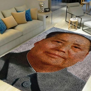 May include: A gray and brown area rug with a portrait of a man's face. The rug is made of a soft, fluffy material.