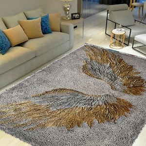 May include: A fluffy gray rug with a gold and gray angel wing design. The rug is in a living room setting with a couch and a side table.