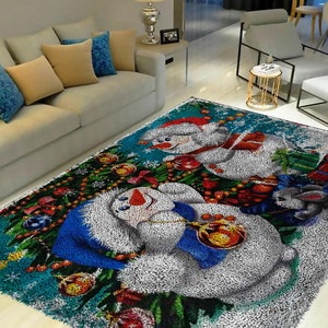 Könnte beinhalten: Ein blaugrüner und weißer, flauschiger Teppich mit einem Weihnachtsmotiv mit zwei Schneemännern, einem Weihnachtsbaum und einem kleinen grauen Kaninchen. Die Schneemänner halten Weihnachtskugeln und der Baum ist mit roten und goldenen Kugeln geschmückt.