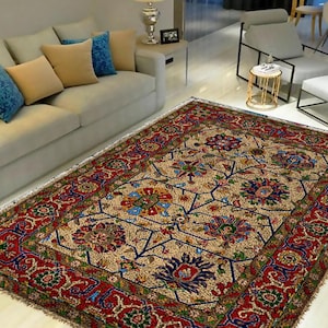 Puede incluir: Una alfombra persa tradicional con fondo crema y intrincados patrones florales en tonos rojos, azules, verdes y dorados. La alfombra tiene una pila gruesa y mullida y un borde con flecos.