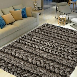 Peut inclure: Un tapis gris tressé avec un poil épais et texturé. Le tapis a un design tissé qui ressemble à un pull en tricot torsadé.