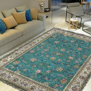 Può includere: Un tappeto blu turchese con un motivo floreale multicolore e un bordo bianco. Il tappeto è in un soggiorno con un divano bianco e cuscini.