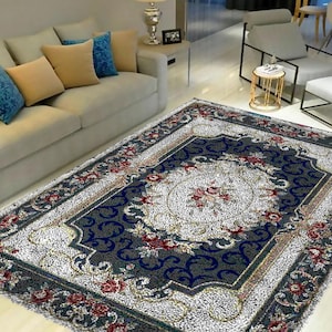 May include: A large, rectangular rug with an ornate floral design. The rug features a central medallion with a floral pattern in shades of red, pink, and cream, surrounded by a dark blue border with scrolling patterns. The rug's edges are trimmed with a decorative border.
