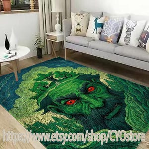 Puede incluir: Alfombra verde y azul con una gran ilustración detallada de la cara de un monstruo verde con ojos rojos. La cabeza del monstruo está cubierta de árboles y follaje.