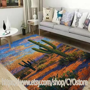 Op de afbeelding: Een kleurrijk vloerkleed met een woestijnlandschap met een grote cactus en kleinere cactussen op de voorgrond. Het kleed heeft een blauwe, oranje en groene kleurstelling.