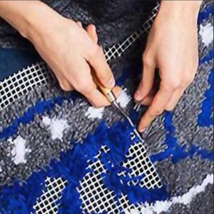 May include: Close-up of a craft project in progress, showing hands using a hook tool to work with yarn on a mesh canvas. The project features a blue, gray, and white color scheme, with a textured, woven appearance.