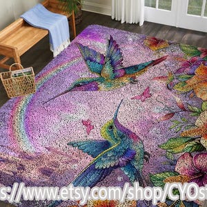 May include: A vibrant, plush rug featuring a colorful hummingbird design. The rug showcases a rainbow, butterflies, and tropical flowers in shades of purple, blue, green, and orange. The Etsy shop URL is visible at the bottom.