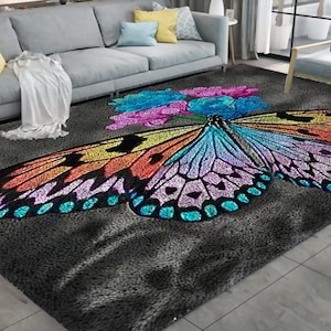 Puede incluir: Una alfombra gris con un diseño de mariposa colorida. La mariposa tiene alas con tonos de azul, morado, naranja y amarillo. La alfombra tiene una textura suave.