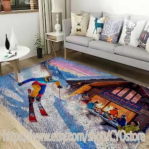 Puede incluir: Una alfombra de área colorida con una escena de invierno que presenta un esquiador, una cabaña de montaña y un grupo de personas. La alfombra tiene un fondo azul, blanco y rosa con una variedad de colores en el diseño.