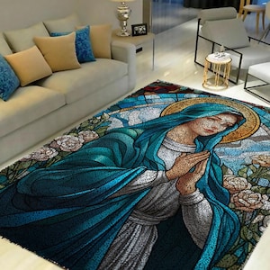May include: A stained glass style rug featuring a blue and white image of the Virgin Mary with a halo, praying with her hands clasped together. The rug has a floral design with white roses and green leaves.