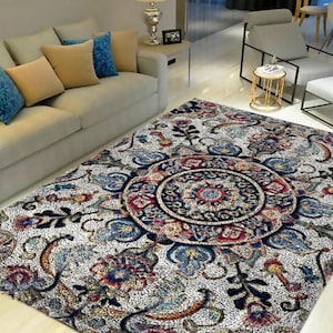 以下が含まれることがあります： 中央に大きくカラフルなマンダラ模様が施された白い敷物。敷物は使い古したようなヴィンテージな風合いがあり、複雑な花柄が特徴です。