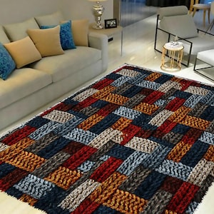 Könnte beinhalten: Ein farbenfroher Teppich mit geometrischem Muster in Blautönen, Rot, Braun und Gold. Der Teppich hat eine gewebte Textur und besteht aus weichen, plüschigen Fasern.