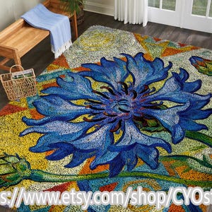 Puede incluir: Una alfombra grande y colorida con un vibrante diseño de flores azules. La alfombra tiene un aspecto texturizado con una mezcla de tonos amarillos, naranjas y verdes. El patrón floral es el punto focal, con una representación detallada de pétalos y tallos.