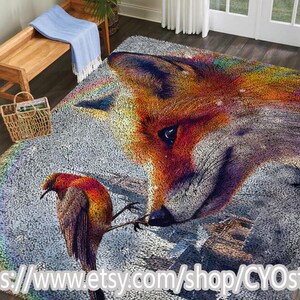 May include: A colorful area rug featuring a detailed illustration of a fox's face and a bird. The fox is depicted with vibrant orange, red, and purple hues, while the bird has orange and brown feathers. The rug has a gray background and a rainbow.