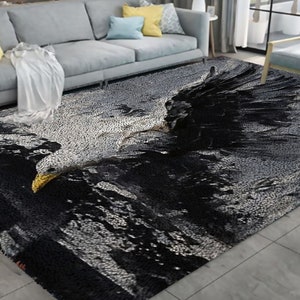 May include: A rectangular area rug featuring a detailed image of an eagle in flight. The rug's design incorporates shades of black, white, and gray, with a yellow beak on the eagle. The rug is placed in a living room setting.
