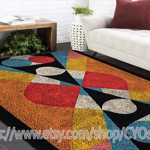 May include: A colorful geometric rug with black, white, red, yellow, blue, and pink circles and triangles. The rug has a textured, fuzzy surface.