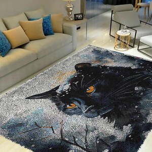 Puede incluir: Una alfombra rectangular con un diseño de pantera negra con ojos de color naranja brillante. La alfombra tiene un efecto de acuarela con tonos de gris, azul y negro. La cara de la pantera es el punto focal, sobre un fondo nevado y texturizado.