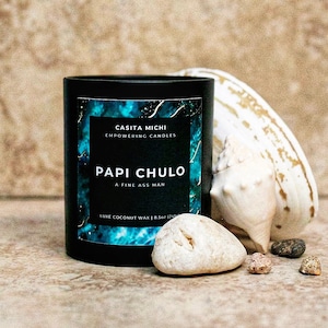 May include: Black candle jar with a blue and gold design. The label reads "Casita Michi Empowering Candles Papi Chulo A Fine Ass Man Luxe Coconut Wax | 8.5oz (241g)"