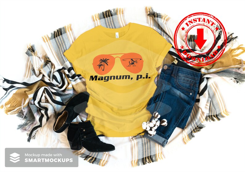 May include: A yellow t-shirt with a graphic of sunglasses and a helicopter with the text "Magnum, p.i." printed on it. The t-shirt is laid out on a blanket with a pair of black boots and blue jeans.