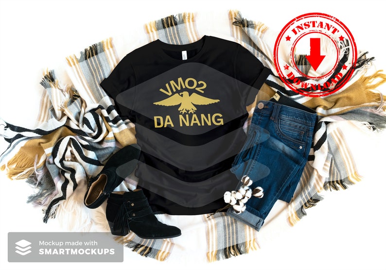 May include: Black t-shirt with a gold eagle graphic and the text "VMO2 DA NANG". The shirt is displayed on a white background with a blanket and jeans.