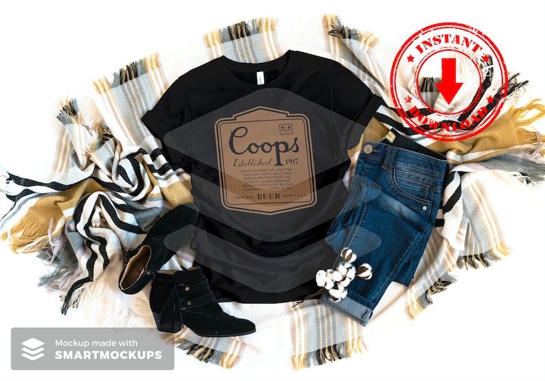 May include: A black t-shirt with a brown label that says "Coops Established 1917 Beer". The t-shirt is on a white background with a blanket and jeans.