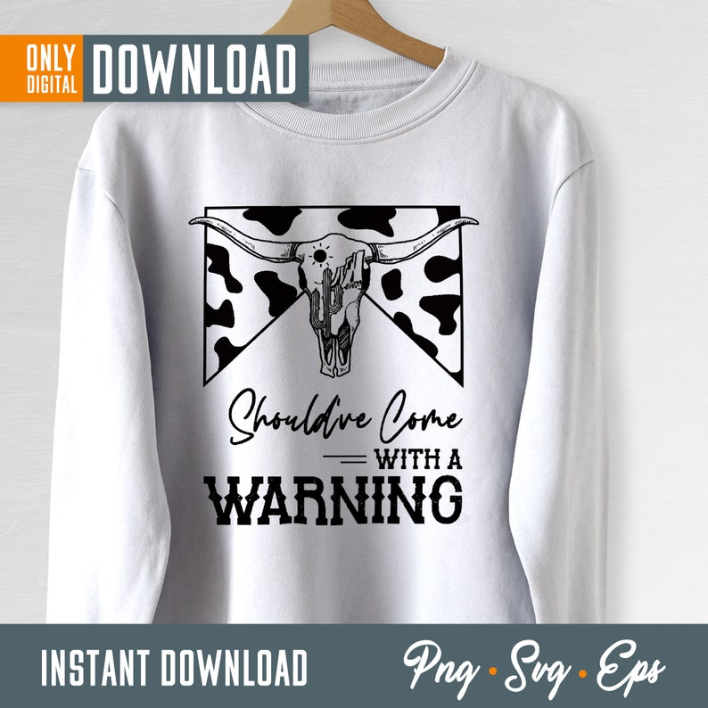 Op de afbeelding: Een wit sweatshirt met een zwart-wit grafisch ontwerp van een koeien schedel met hoorns en een cactus. De tekst "Should've Come With A Warning" staat onder de schedel.
