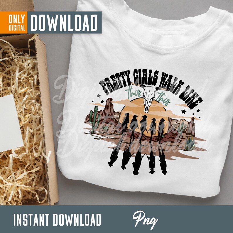 May include: A white t-shirt with a graphic design of a sunset scene with cacti and a cow skull. The text "Pretty Girls Walk Like This" is written in a green and black font around the graphic.