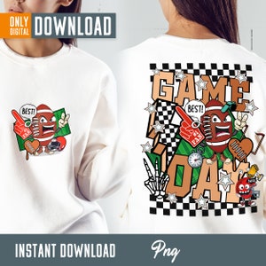 Op de afbeelding: Een wit sweatshirt met een cartoon voetbalpersonage en de tekst "GAME DAY" op de rug. Het voetbalpersonage draagt een hoed en houdt een rode schuimvinger vast. De tekst is in een zwart-wit geruit patroon met sterren en andere graphics.