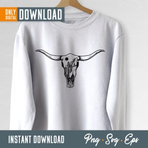 Op de afbeelding: Een wit sweatshirt met een zwart-witte illustratie van een stieren schedel met een cactus en zon erin. De tekst "Download" staat in de rechterbovenhoek van de afbeelding. De tekst "Instant Download" staat in de linkerbenedenhoek van de afbeelding. De tekst "Png - Svg - Eps" staat in de rechterbenedenhoek van de afbeelding.