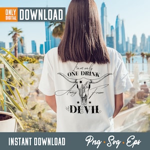Op de afbeelding: Wit T-shirt met een zwarte afbeelding van een schedel met hoorns en de tekst "Ik ben maar &eacute;&eacute;n drankje verwijderd van de duivel".