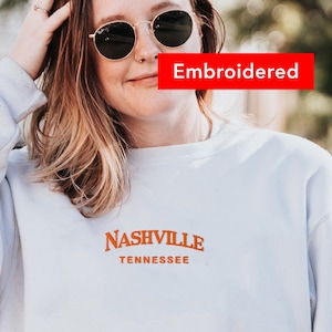 May include: White sweatshirt with an orange embroidered design that says "Nashville Tennessee".