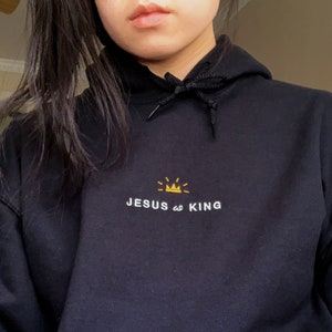 以下が含まれることがあります： 「JESUS is KING」という白い文字と、KINGの文字の上に金色の王冠がついた黒いフード付きスウェットシャツ。