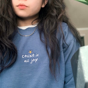 May include: A blue sweatshirt with the text "count it all joy" embroidered on the front. A small yellow star is above the text.