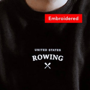 Puede incluir: Sudadera negra con el texto bordado "UNITED STATES ROWING" y un par de remos cruzados.