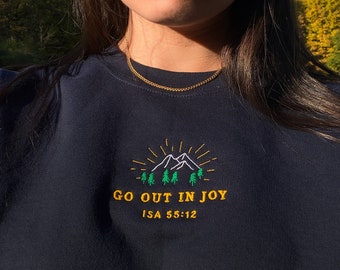 Könnte beinhalten: Ein schwarzer Pullover mit einem gestickten Design aus Bergen und Bäumen in Grün und Weiß. Der Text "GO OUT IN JOY ISA 55:12" ist in Gelb unter dem Design gestickt.