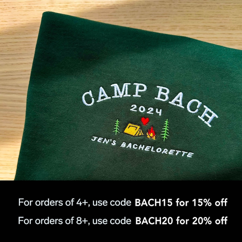 May include: Green sweatshirt with embroidered text "CAMP BACH 2024" and a small camping scene with a tent, fire, and heart. The text "JEN'S BACHELORETTE" is also embroidered below the scene. The text "For orders of 4+, use code BACH15 for 15% off" and "For orders of 8+, use code BACH20 for 20% off" is printed below the image.