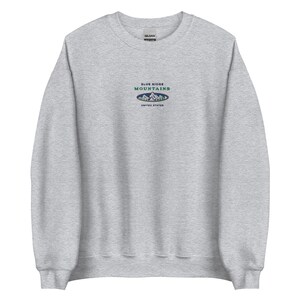 Op de afbeelding: Een grijs sweatshirt met een blauw en groen geborduurd logo met de tekst "Blue Ridge Mountains" en "United States".