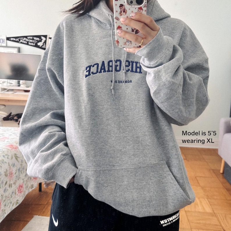 May include: Grey oversized hoodie with a blue embroidered logo that reads "HIS GRACE" in reverse. The model is wearing a size XL.