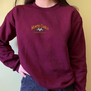 May include: Burgundy sweatshirt with a gold embroidered logo that says "Monte Carlo Country Club" with a tennis racket graphic.