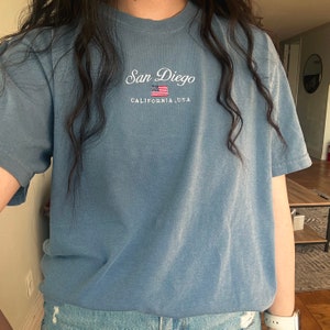 May include: A light blue t-shirt with the text "San Diego, California, USA" and a small American flag embroidered on the front.